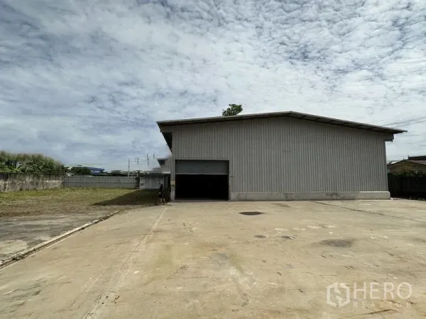 Warehouse for rent in Min Buri, Bangkok - Metal-clad warehouse with an open roller shutter and a wide concrete loading yard.