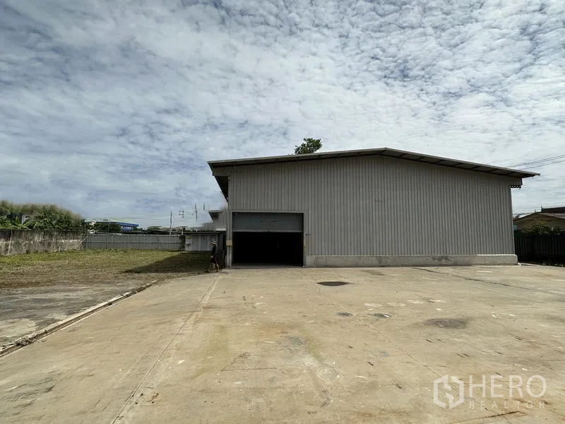 Warehouse for rent in Min Buri, Bangkok - Metal-clad warehouse with an open roller shutter and a wide concrete loading yard.
