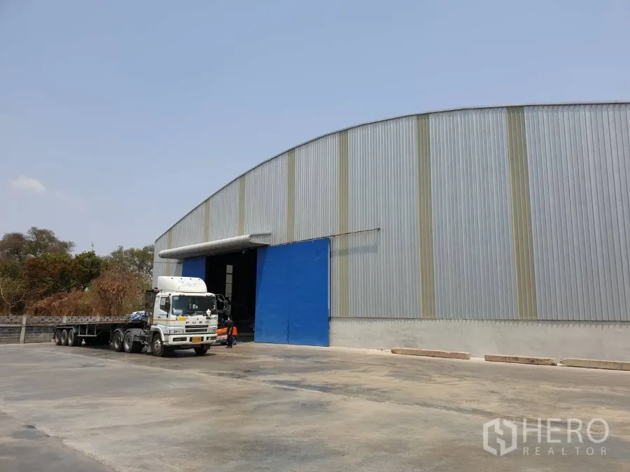 Warehouse for rent in Chaloem Phra Kiat, Saraburi - Side view of a large industrial warehouse with a blue entry and spacious paved turning area suitable for trailers in Saraburi.