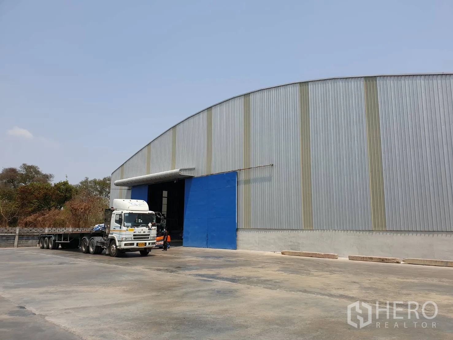 Warehouse for rent in Chaloem Phra Kiat, Saraburi - Side view of a large industrial warehouse with a blue entry and spacious paved turning area suitable for trailers in Saraburi.
