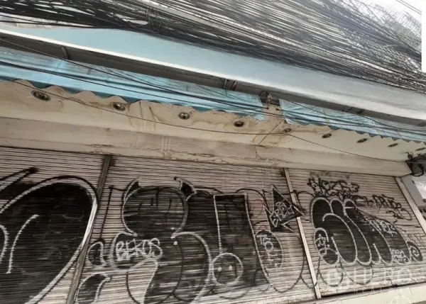 อาคารพาณิชย์ ให้เช่าในWatthana, Bangkok - หน้าร้านตึกแถวประตูม้วนปิดมีกราฟฟิตี หลังคากันสาด และสายสื่อสารจำนวนมากเหนือศีรษะ