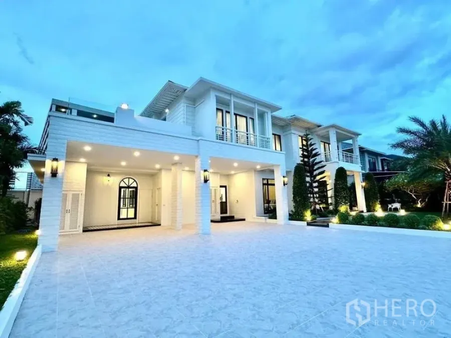 Detached House for rent in Bang Phli, Samut Prakan - Front facade of the white luxury house with expansive parking and trimmed greenery.