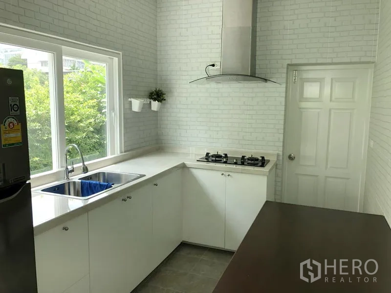 Detached House for rent or sale in Huai Khwang, Bangkok - Bright white L-shaped kitchen with gas hob, extractor hood and a window over the sink.