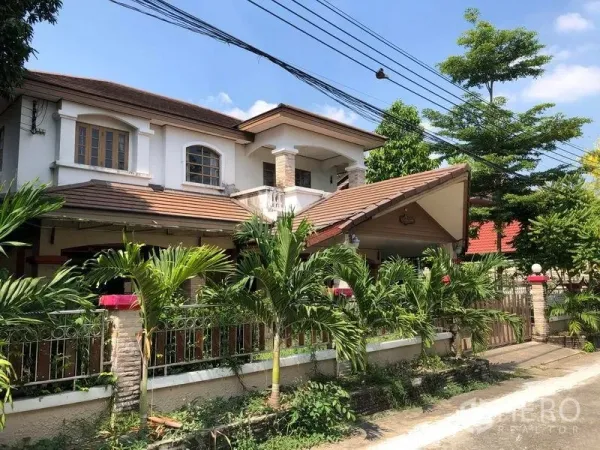 Detached House for sale in Pak Kret, Nonthaburi - Angled exterior of the Pak Kret detached house showing covered carport, brick-clad pillars, metal gate and tropical landscaping along the wall.