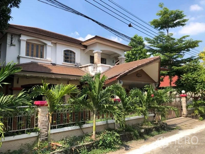 Detached House for sale in Pak Kret, Nonthaburi - Angled exterior of the Pak Kret detached house showing covered carport, brick-clad pillars, metal gate and tropical landscaping along the wall.