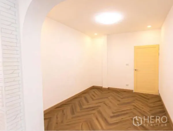 Detached House for sale in Wang Thonglang, Bangkok - Empty room with white walls, herringbone wood floors and a pale wooden door under recessed lights.