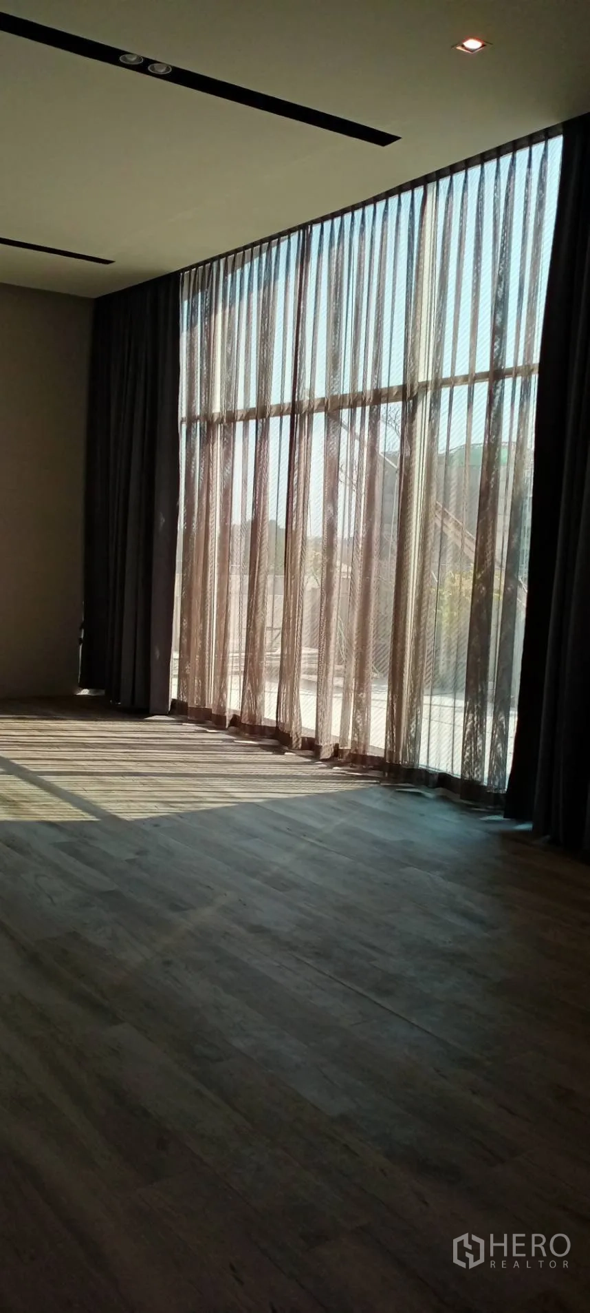 สำนักงาน ให้เช่า - กระจกเต็มความสูงพร้อมผ้าม่านโปร่ง แสงอาทิตย์ทอดเงาบนพื้นไม้.