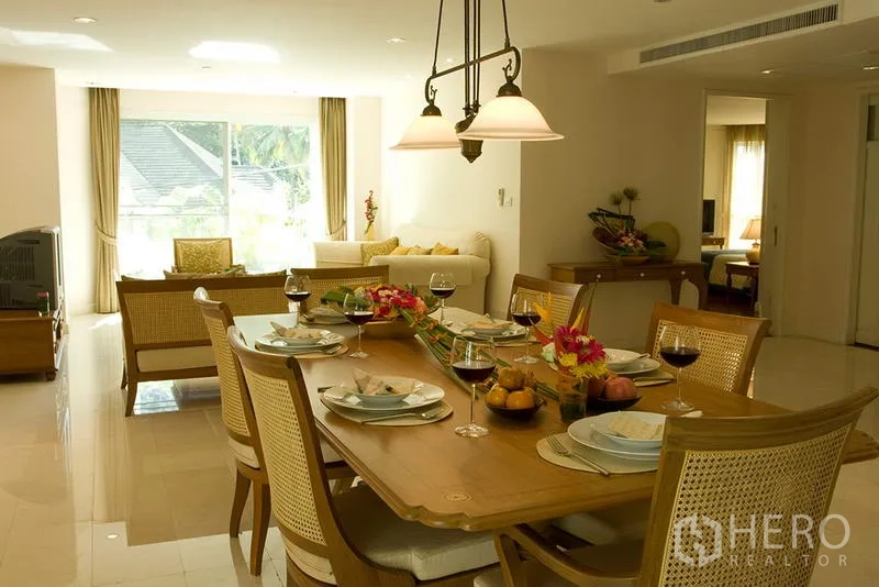 Apartment for rent in Bang Rak, Bangkok - Bright open-plan dining and living area with wooden table, pendant lights and large window in a Silom apartment.