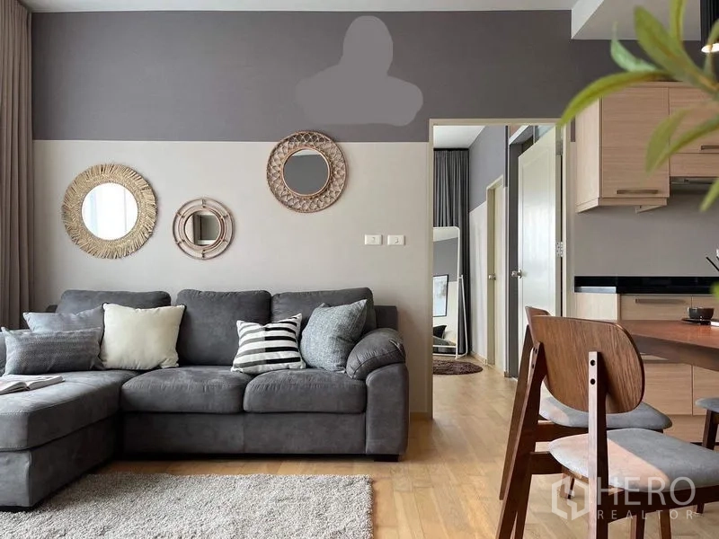 คอนโด ให้เช่าในWatthana, Bangkok - ห้องนั่งเล่นโทนเทา โซฟาตัวแอล กระจกตกแต่งผนัง และทางเชื่อมไปยังห้องนอนกับครัว