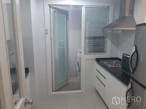 คอนโด ให้เช่าในKhlong Toei, Bangkok - ครัวปิดสว่างพร้อมท็อปสีดำ เตาและเครื่องดูดควัน ประตูกระจกเปิดสู่โซนซักล้างที่มีเครื่องซักผ้า