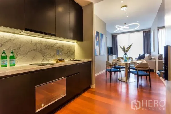 公寓 出租在Watthana, Bangkok - 深色柜体的现代厨房，配大理石背板和橱柜下灯，旁接餐区。