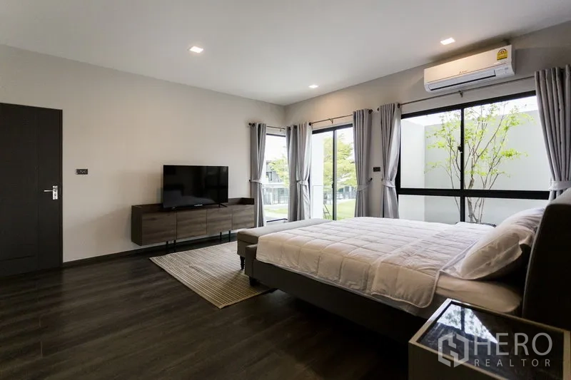 联排别墅 出租在Samut Prakan - 主卧另一角度，电视柜、转角窗与空调。