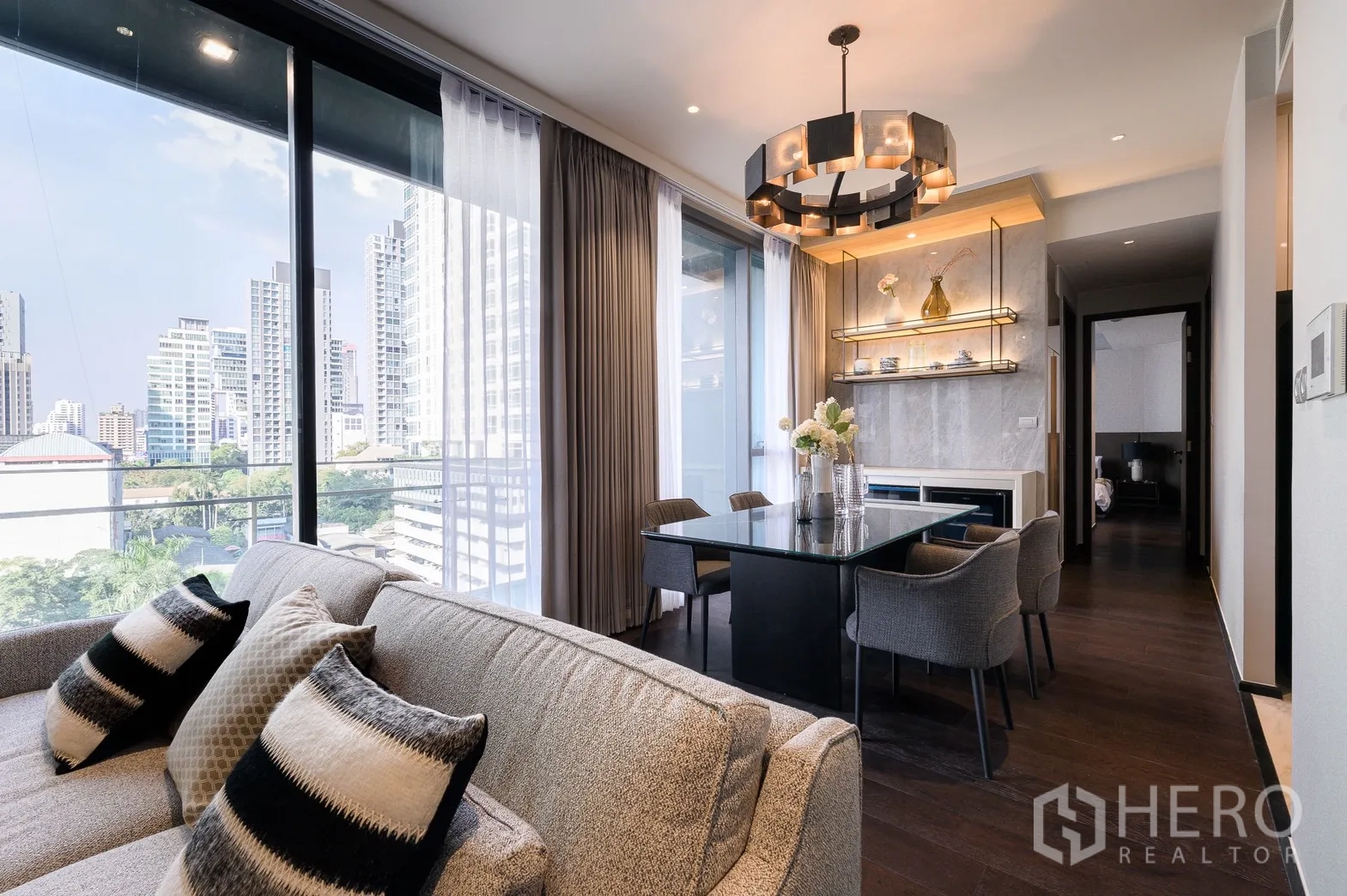 Condominium for rent or sale in Watthana, Bangkok - Open living and dining area with skyline views, statement chandelier and corridor leading to bedrooms.