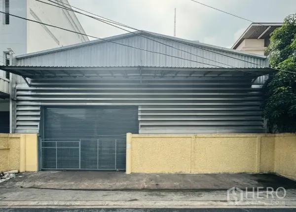 Warehouse for rent in Din Daeng, Bangkok - Front elevation of the warehouse showing the closed rolling shutter, metal gate and canopy.