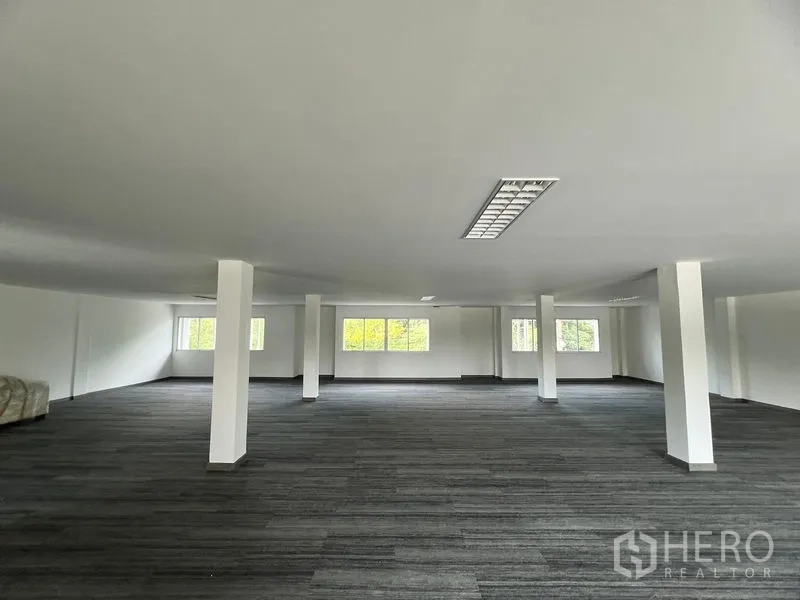 零售空间 出租在Huai Khwang, Bangkok - 开放式零售楼层，白色立柱、地毯地面与吊顶灯具，多扇窗户带来自然采光。