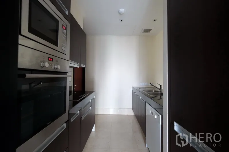 Condominium for rent in Bang Rak, Bangkok - Galley kitchen with built-in oven, microwave, cooktop, dishwasher and double sink.
