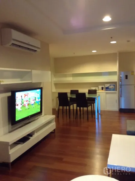Condominium for rent in Huai Khwang, Bangkok - Living and dining space with wall-mounted TV, built-in shelving and recessed lighting.