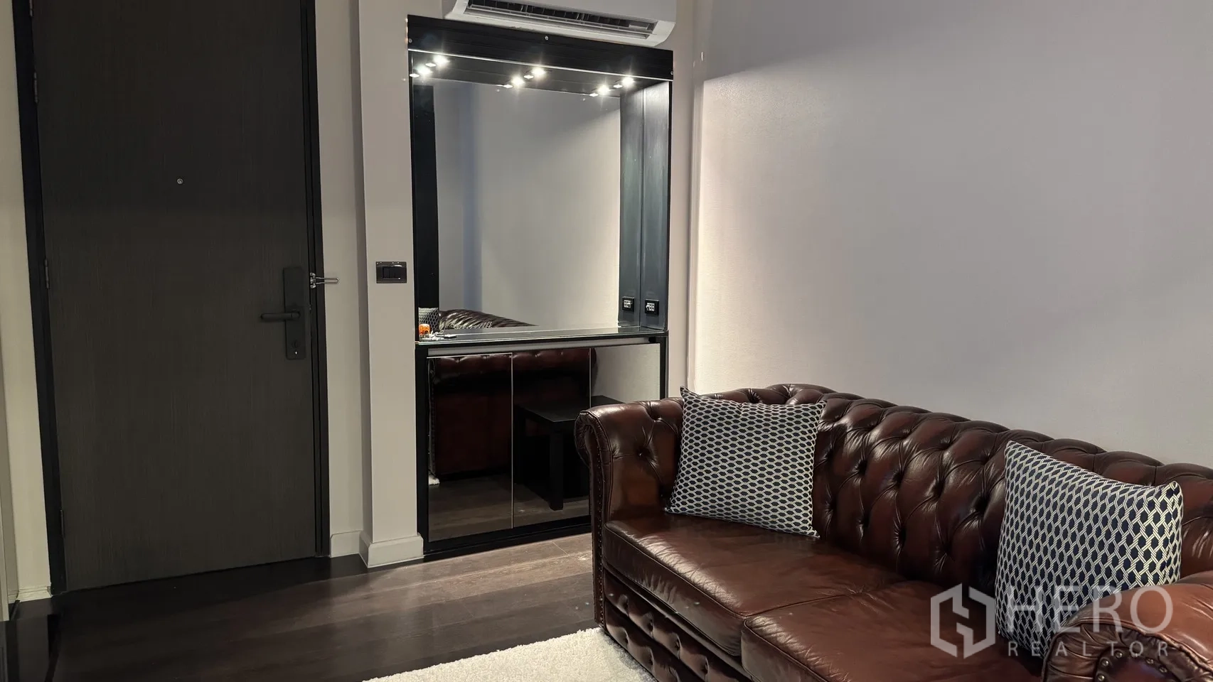 公寓 出租或出售在Khlong Toei, Bangkok - 玄关区设大镜面与棕色皮沙发，深色木地板质感温暖。