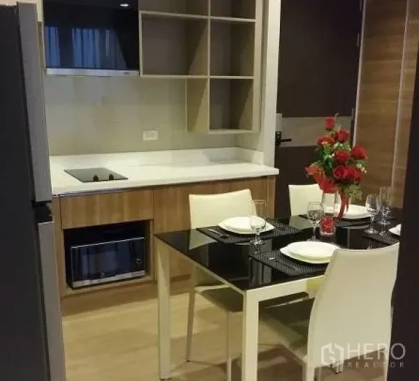 Condominium for rent in Sathon, Bangkok - Compact kitchen with built-in hob, microwave, open shelving and a black glass dining table.