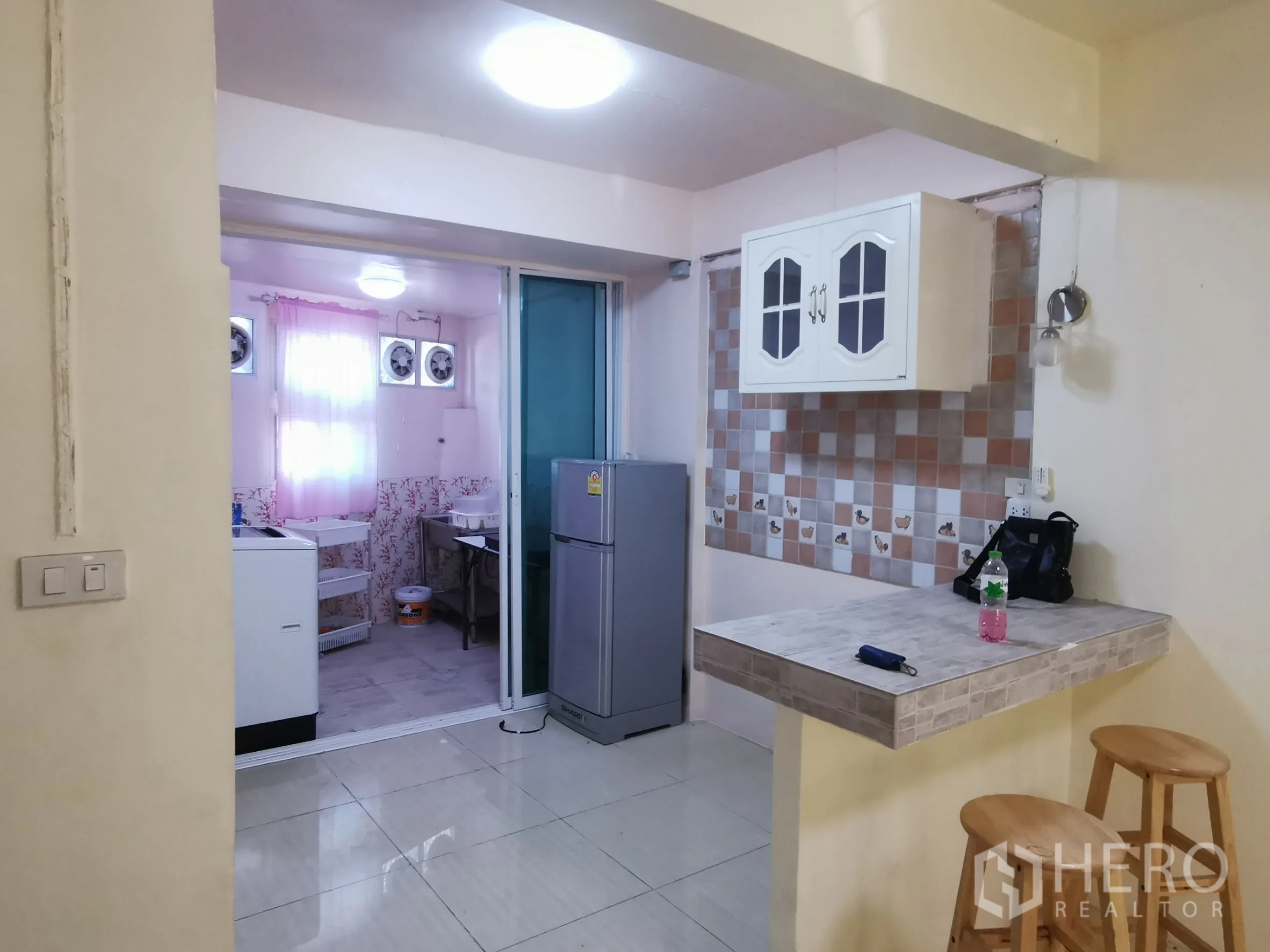 ทาวน์เฮาส์ ให้เช่าในKhlong Toei, Bangkok - มุมครัวผนังกระเบื้องลายตาราง ตู้แขวน เคาน์เตอร์บาร์ และประตูกระจกบานเลื่อนไปยังโซนซักล้าง