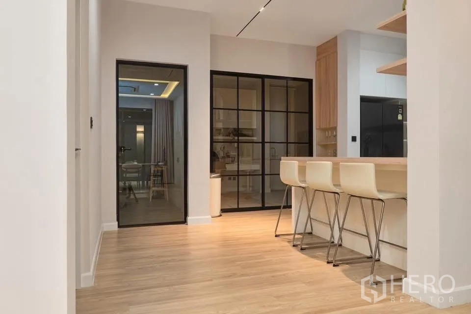 独栋房屋 for rent in Phra Khanong, Bangkok - 走廊望向厨房，黑框玻璃门与吧台高脚椅。