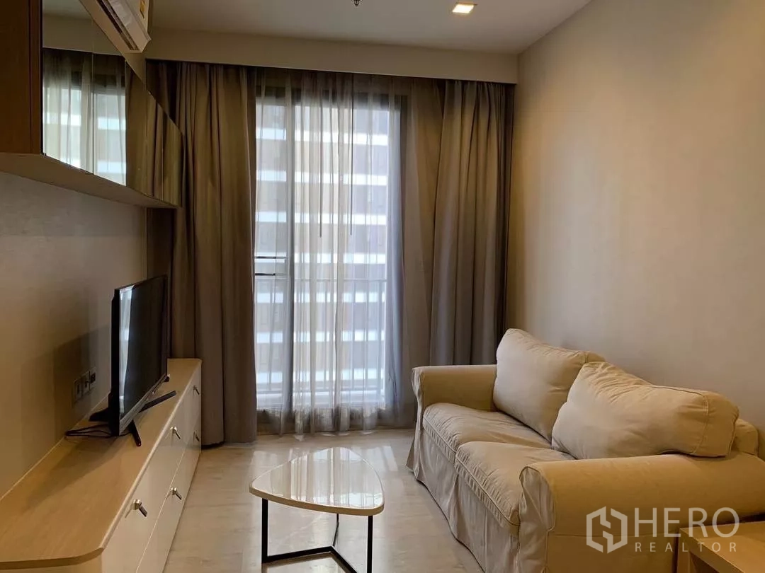 Condominium for rent or sale in Watthana, Bangkok - Bright living room with beige sofa, TV console and floor-to-ceiling curtains in an Ekkamai condo.