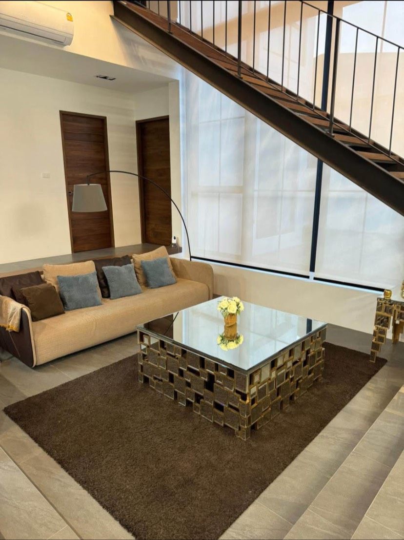 บ้าน ขายในKhlong San, Bangkok - ห้องนั่งเล่นอบอุ่นใต้บันไดโลหะ โซฟาสีเบจ โต๊ะกลางกระจก และมู่ลี่โปร่งแสง
