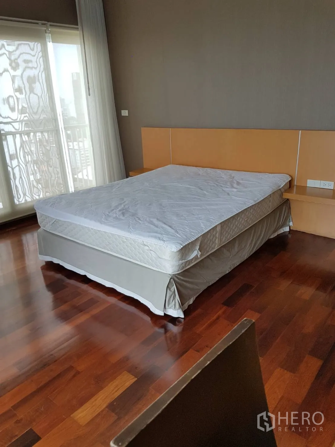 Condominium for rent or sale in Watthana, Bangkok - Primary bedroom with hardwood floors, built-in headboard, and balcony doors with sheer curtains.