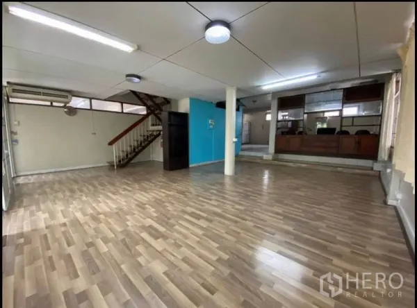 Home Office for rent in Suan Luang, Bangkok - Expansive room with laminate floors, a blue feature wall, staircase and reception-style glass partition.