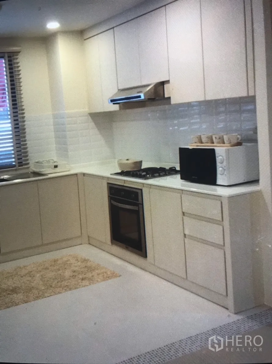 公寓 出租在Bang Rak, Bangkok - 浅色L型厨房，白色橱柜、燃气灶、嵌入式烤箱、抽油烟机与微波炉。