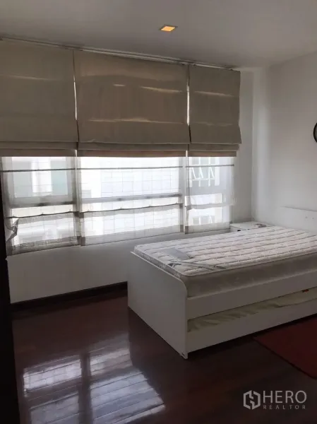 Condominium for rent in Watthana, Bangkok - Sunlit bedroom with dark wood floors, roman blinds and a white bed frame in a Watthana Bangkok condominium.