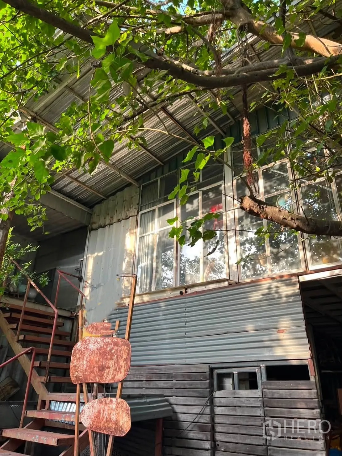 โกดัง for rent in Watthana, Bangkok - ด้านข้างอาคารแผ่นลอนเหล็ก บันไดนอกอาคาร และช่องหน้าต่างใต้ร่มไม้