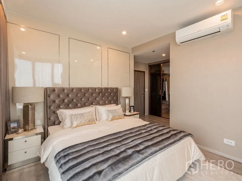 Condominium for rent in Bang Na, Bangkok - Master bedroom angle showing air-conditioning, bedside tables and doorway to the closet.