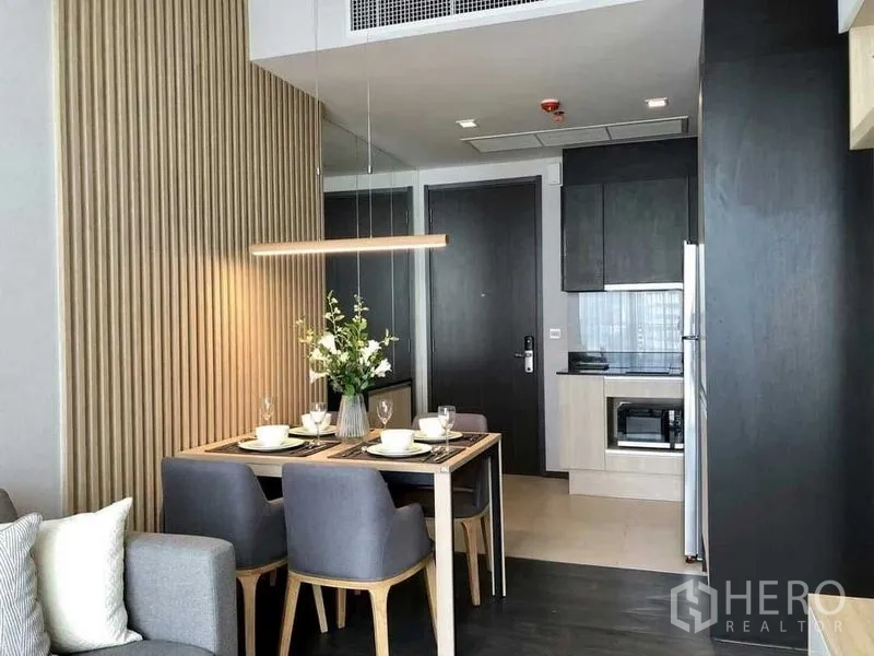 Condominium for rent in Watthana, Bangkok - Modern kitchenette with built‑in cabinetry, microwave and a dining table under a linear pendant light.