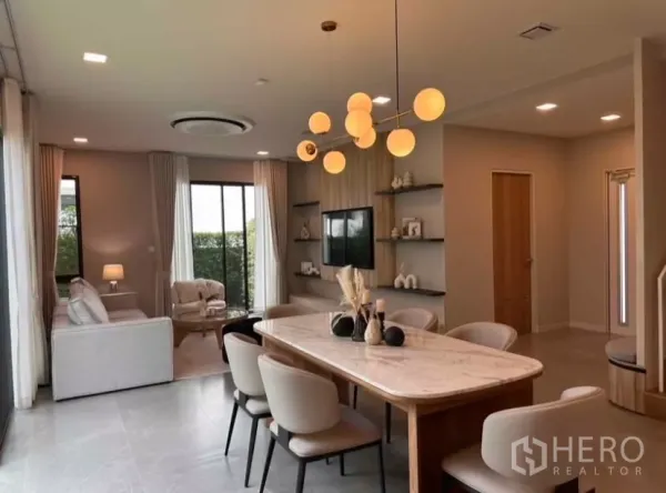 Detached House for rent in Samut Prakan - Open-plan dining and lounge with marble table, statement chandelier, and built-in TV wall.