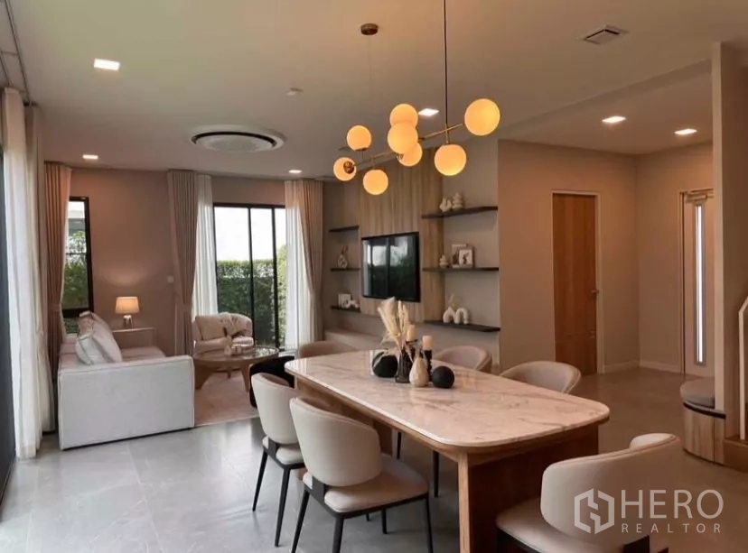 Detached House for rent in Samut Prakan - Open-plan dining and lounge with marble table, statement chandelier, and built-in TV wall.