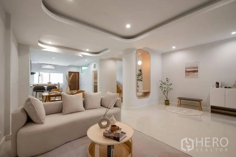 联排别墅 出售在Khlong Toei, Bangkok - 开放式客餐厅，曲线吊顶、柔和灯光与米色沙发，后接餐区。