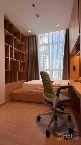 Condominium for rent in Bang Rak, Bangkok - Cozy bedroom with platform bed, built-in desk and shelving, and a tall window offering a city view.