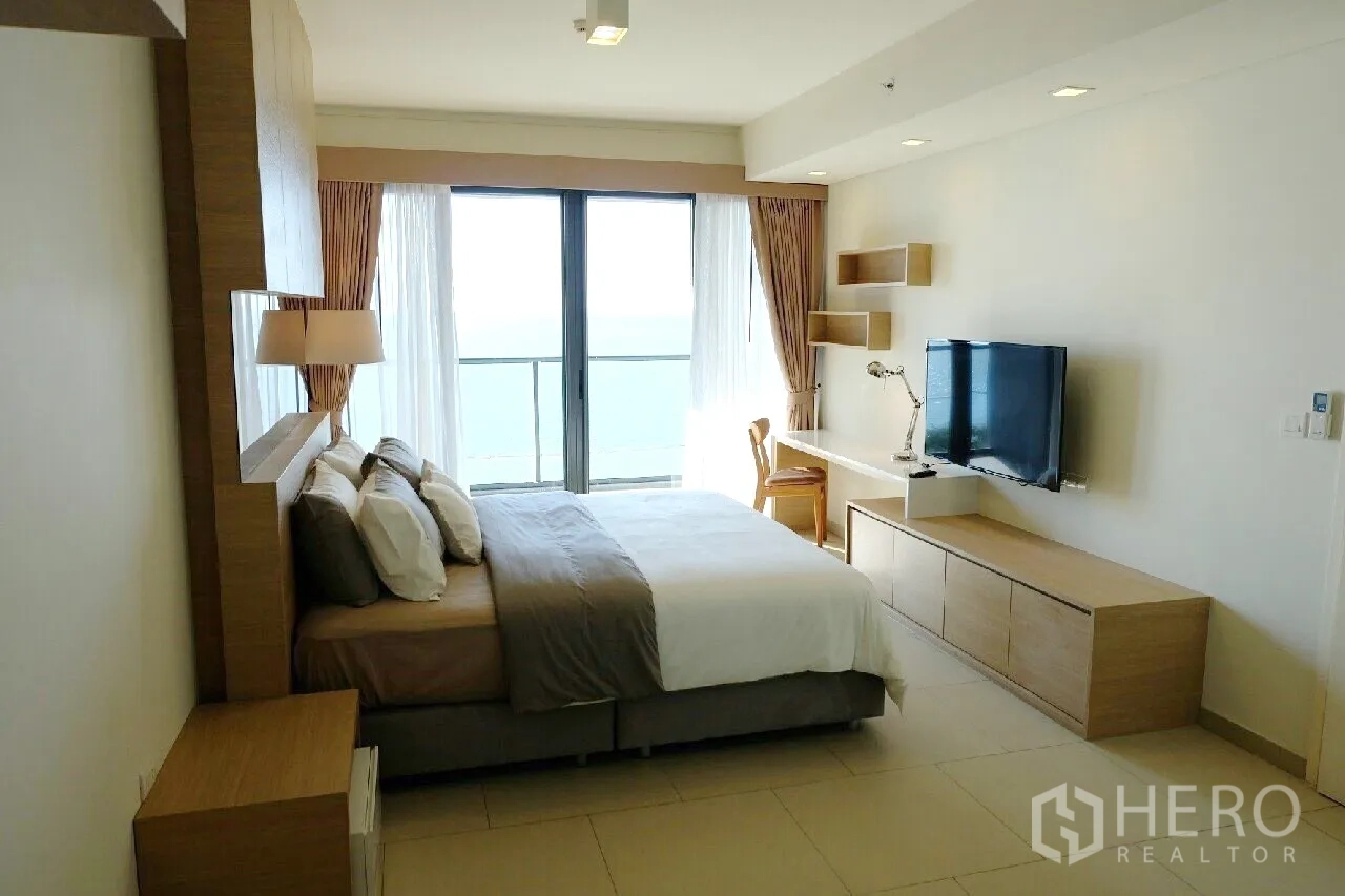 Condominium for rent or sale in Bang Lamung, Chon Buri - Spacious bedroom suite with TV, study desk and sliding doors to a sea-view balcony.
