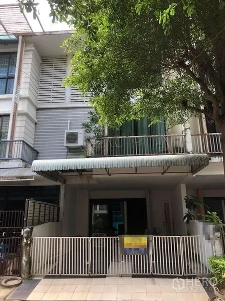 ทาวน์เฮาส์ ขาย - มุมมองด้านหน้าแสดงรั้วเหล็ก ประตูกระจกบานเลื่อน ระเบียงและกันสาด ภายใต้ต้นไม้ใหญ่