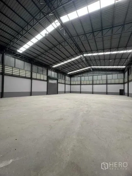 工厂 出售在Samut Sakhon - 高挑仓库内部，钢结构桁架、天窗采光与平整混凝土地面。