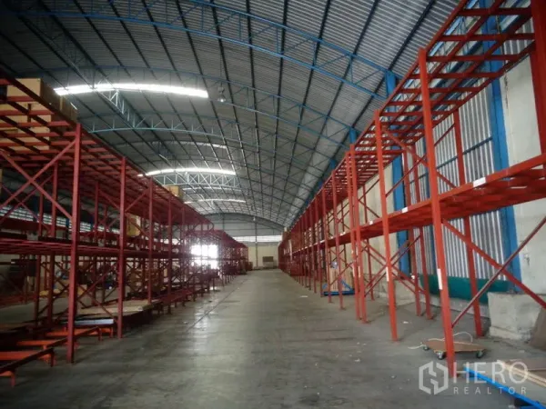 Warehouse for rent or sale in Lat Lum Kaeo, Pathum Thani - Long central aisle between red pallet racking beneath a clear-span metal roof.
