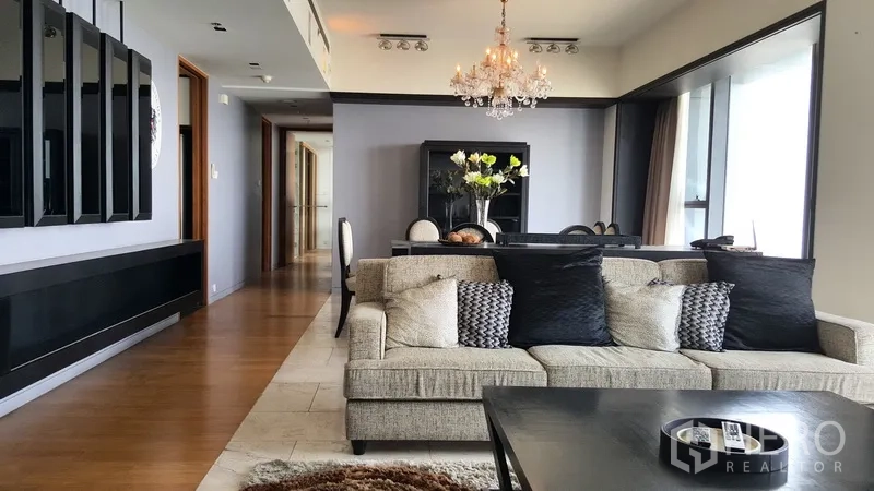 Condominium for rent in Sathon, Bangkok - Spacious lounge with plush sofa, hallway to bedrooms, and elegant dining set under a crystal chandelier.