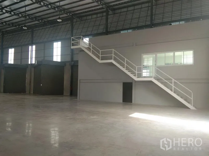 คลังสินค้า ให้เช่าในBang Phli, Samut Prakan - สำนักงานชั้นลอยภายใน พร้อมบันไดเหล็กสีขาว มองเห็นพื้นโกดังและประตูม้วนหลายบาน