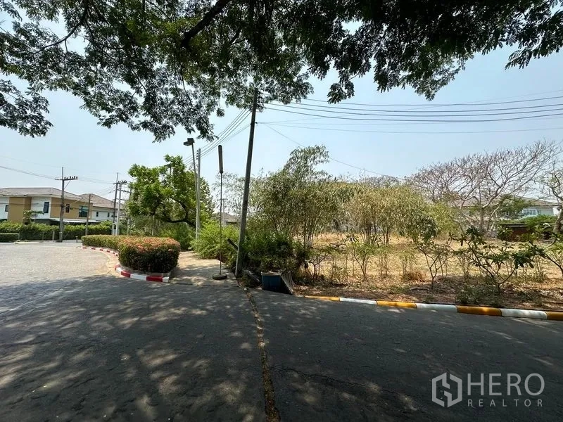 Land for sale in Khlong Luang, Pathum Thani - Corner of an internal road with streetlights and access to a vacant plot; cables overhead.