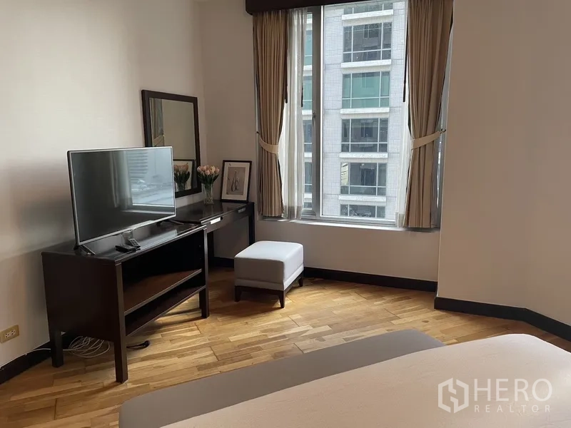 Condominium for rent or sale in Pathum Wan, Bangkok - Bedroom corner with TV console, desk, mirror and a window facing nearby buildings.