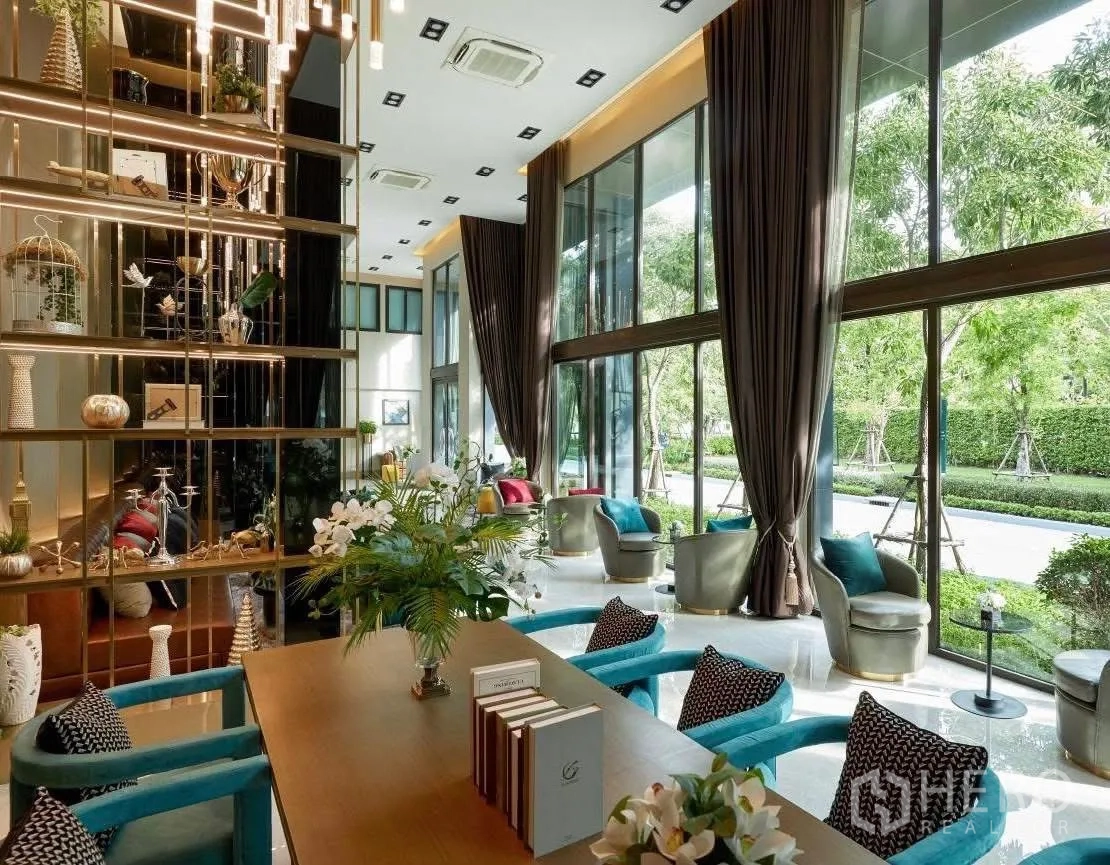 Detached House for rent or sale in Wang Thonglang, Bangkok - Double-height clubhouse lounge with floor-to-ceiling windows, plush seating and decorative shelves.