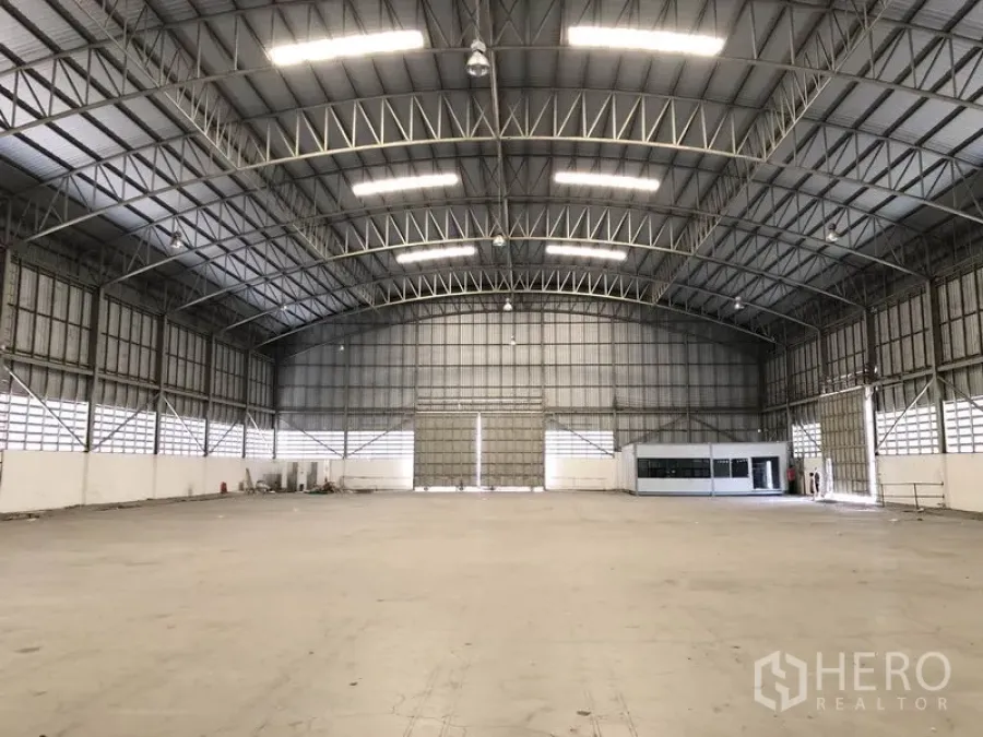 Warehouse for rent in Pathum Thani - Bright open warehouse hall with illuminated steel rafters, roller doors and an internal office box.