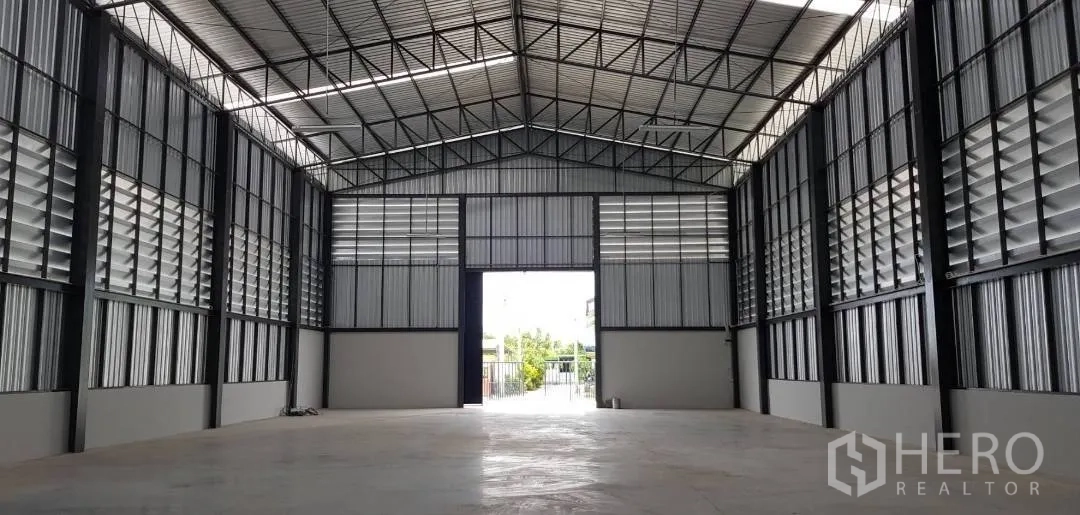 Warehouse for rent in Mueang Samut Prakan, Samut Prakan - Warehouse interior with a high steel truss roof, large entry door, and concrete floor.