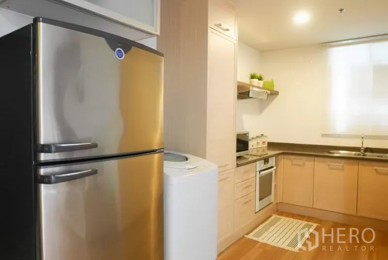 Condominium for rent in Pathum Wan, Bangkok - Kitchen view showing stainless refrigerator and washing machine beside built-in cabinets.